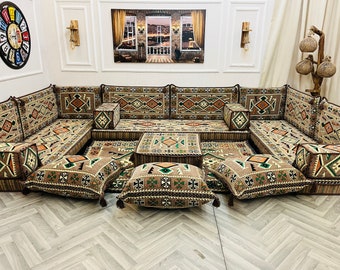 May include: A traditional Middle Eastern seating arrangement with a large, L-shaped sofa covered in a brown and beige patterned fabric. The sofa is made up of multiple cushions and has a matching patterned rug underneath. There are several smaller cushions scattered around the sofa, all with intricate geometric designs.