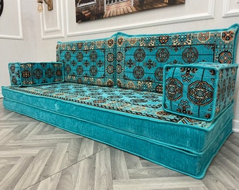 May include: A turquoise blue floor cushion sofa with patterned cushions. The sofa has a traditional design with a geometric pattern and is perfect for a living room or bedroom.