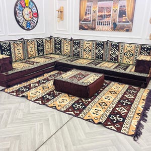 Puede incluir: Un sofá seccional marrón y beige con estampado con una alfombra estampada a juego y un otomano marrón. El sofá está formado por varios cojines y tiene un diseño tradicional.