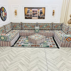 May include: A gray and white patterned sectional sofa with a matching ottoman. The sofa is made up of individual cushions and has a traditional design. The sofa is set on a light gray wood floor.