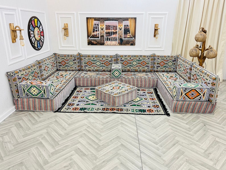 May include: A gray and white patterned sectional sofa with a matching ottoman. The sofa is made up of individual cushions and has a traditional design. The sofa is set on a light gray wood floor.