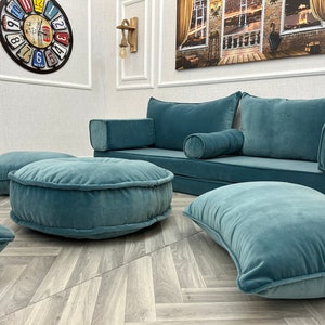 May include: A teal blue sofa with matching throw pillows and floor cushions. The sofa has a low back and is perfect for lounging. The floor cushions are round and have a tufted design.