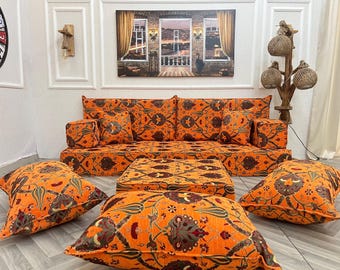 May include: A traditional orange and brown patterned floor seating set with a sofa, cushions, and a coffee table. The sofa has a high back and is covered in a floral patterned fabric. The cushions are also covered in the same fabric. The coffee table is a square shape and is also covered in the same fabric.