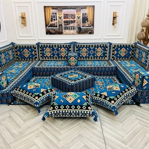Op de afbeelding: Een blauwe en beige gepatroneerde hoekbank met meerdere kussens en een bijpassende ottomane. De bank is in een U-vorm gerangschikt en is perfect voor een woonkamer of familiekamer.