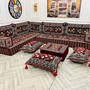 May include: A red and black patterned sectional sofa with matching throw pillows and a small red ottoman. The sofa is arranged in a U-shape and is decorated with intricate embroidery.