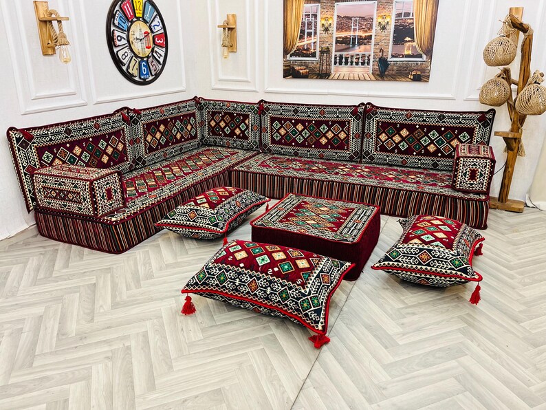 May include: A red and black patterned sectional sofa with matching throw pillows and a small red ottoman. The sofa is arranged in a U-shape and is decorated with intricate embroidery.