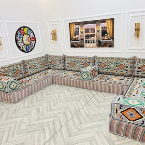May include: A large, gray and white patterned sectional sofa with a geometric design. The sofa is made up of multiple cushions and has a small, square ottoman in the center.