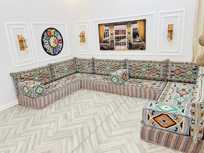 May include: A large, gray and white patterned sectional sofa with a geometric design. The sofa is made up of multiple cushions and has a small, square ottoman in the center.