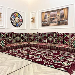 May include: A traditional Middle Eastern floor seating arrangement with a burgundy and cream patterned rug. The seating is made up of multiple cushions with a geometric pattern in shades of burgundy, cream, and green.