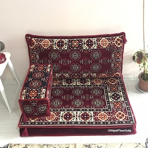 May include: A red, orange, and cream patterned floor sofa with a matching armrest cushion. The sofa has a burgundy border and tassels.