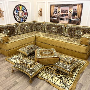May include: A sectional sofa with a gold base and patterned cushions and backrests. The cushions and backrests have a brown and gold floral design. The sofa is accompanied by matching pillows and a rug, creating a cohesive living room set.