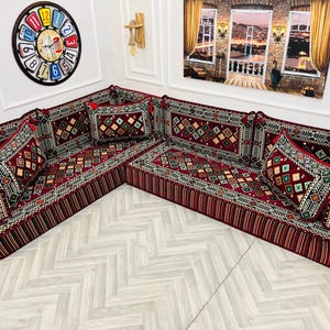 May include: A red and gold patterned sectional sofa with multiple pillows. The sofa is made of fabric and has a traditional design.