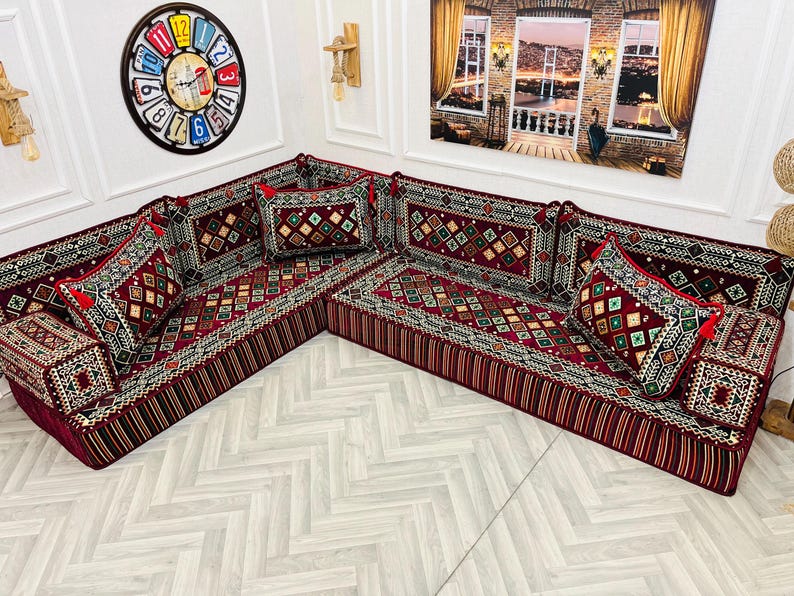 May include: A red and gold patterned sectional sofa with multiple pillows. The sofa is made of fabric and has a traditional design.