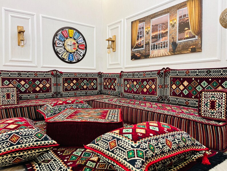 May include: A red and gold patterned floor cushion set with a variety of cushions and pillows. The cushions are arranged in a traditional seating style, with a large central cushion and smaller cushions around it. The cushions are made of a soft, plush fabric and have a variety of intricate patterns.