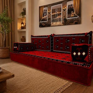 May include: A floor sofa set featuring a long rectangular base cushion in deep red with black and white geometric patterns. The set includes matching backrest cushions and square side pillows, all adorned with intricate traditional embroidery.
