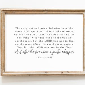 May include: A framed print featuring a quote from 1 Kings 19:11-12, set against a white backdrop. The text is in black, using a combination of serif and script fonts. The frame is a light brown, rectangular design.