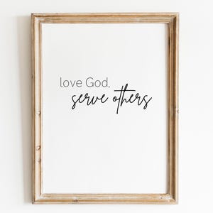 Könnte beinhalten: Ein gerahmter Druck mit dem Text "love God, serve others" in schwarzer Kursivschrift auf weißem Hintergrund.