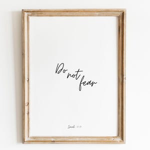 May include: A framed print featuring the phrase "Do not fear" in black cursive script on a white background. The print is enclosed in a light brown, wooden frame with a rustic finish. The scripture reference Isaiah 41:10 is at the bottom.