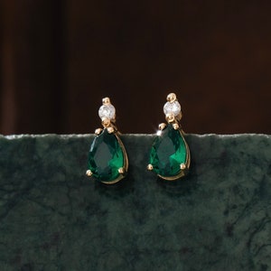 Könnte beinhalten: Ein Paar goldene Ohrringe mit tropfenförmigen grünen Edelsteinen und kleinen klaren Steinen.