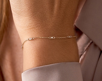 May include: A delicate gold chain bracelet with small, clear gemstones. The bracelet is worn on a person's wrist.