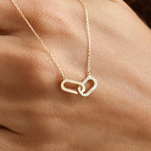 May include: A delicate gold necklace featuring two interlocking oval pendants. One pendant is solid gold, while the other is encrusted with small, sparkling gemstones. The necklace is displayed on a person's hand.