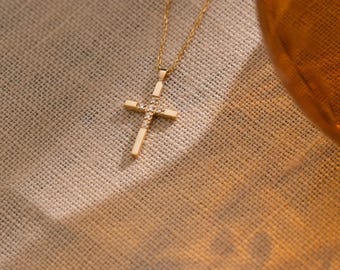 May include: A gold-toned necklace featuring a delicate chain and a cross pendant. The cross is embellished with small, clear, sparkling stones set along its vertical and horizontal bars, creating a refined and polished appearance.