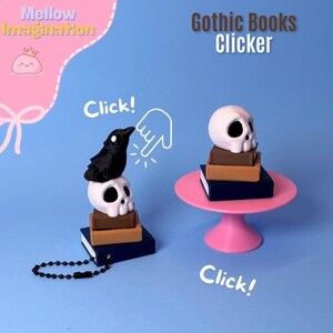 May include: A whimsical, pink and blue image featuring miniature gothic-themed book clickers. One clicker has a black raven perched atop a white skull, stacked on books. The other has a skull on a pink stand. Text reads "Gothic Books Clicker."