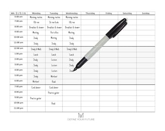 May include: A black and white weekly planner with a black marker on top of it. The planner has a grid layout with days of the week listed across the top and times listed down the side. The planner has the text "Wk: 01/01/21" in the top left corner and "DEFINE YOUR FUTURE" in the bottom center.