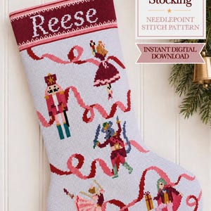 May include: A needlepoint Christmas stocking pattern featuring the name Reese at the top. The design includes a nutcracker, a ballerina, and a mouse king character, all connected by a flowing pink ribbon on a white grid background.