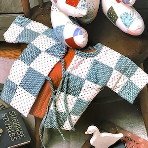 May include: A baby's quilted jacket with a checkered pattern in shades of blue and white. The jacket has a tie closure and is made of a soft, comfortable fabric.