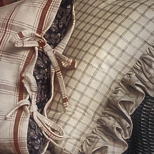 以下が含まれることがあります： 白と茶色の格子模様の枕で、フリルが付いています。枕は白と茶色の格子模様で、茶色のリボンが結ばれています。