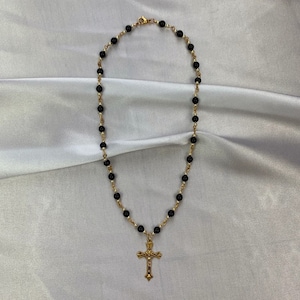 May include: A gold chain necklace with black beads and a gold cross pendant.