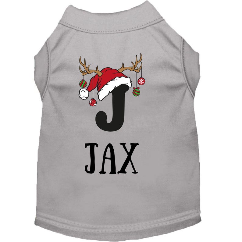 May include: A gray dog shirt with a red Santa hat, antlers, and ornaments. The letter J and the name Jax are printed on the shirt.
