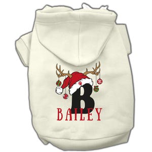 May include: White dog hoodie with a red Santa hat and antlers with ornaments hanging from them. The letter "B" and the name "BAILEY" are printed on the hoodie.