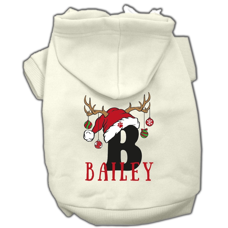 May include: White dog hoodie with a red Santa hat and antlers with ornaments hanging from them. The letter "B" and the name "BAILEY" are printed on the hoodie.