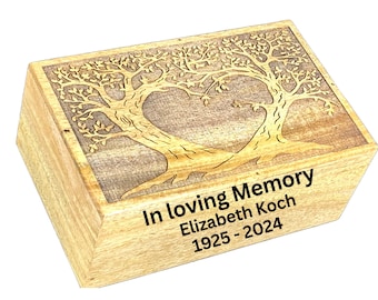 May include: A wooden box with a carved tree design on the lid. The box is light brown with a rectangular shape. The text "In loving Memory Elizabeth Koch 1925-2024" is printed on the front.