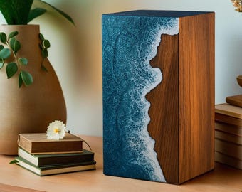 May include: A rectangular wooden box with a distinctive design. One side showcases a blue resin ocean wave design with a white, foamy edge. The other side displays natural wood grain. The box is on a wooden surface.