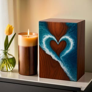 May include: A wooden cremation urn with a heart-shaped wave design in blue and white. A tall, lit candle and a vase with a yellow tulip are next to the urn. The urn is rectangular and made of wood.
