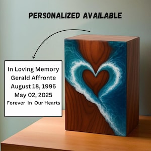 May include: A wooden urn featuring a heart design. The heart is created by a blue and white wave pattern set against a brown wood grain. Text on the left reads "In Loving Memory Gerald Affronte August 18, 1995 May 02, 2025 Forever In Our Hearts."