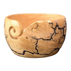 May include: A wooden yarn bowl with a natural wood finish and black crackle design. The bowl has a carved spiral yarn guide.