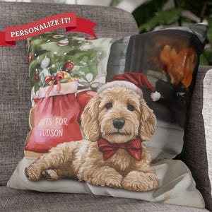 May include: A throw pillow with a Christmas-themed design featuring a dog wearing a Santa hat and a red bow tie. The dog is sitting in front of a fireplace with a Christmas tree in the background. The pillow has the text "Gifts for Hudson" on it.