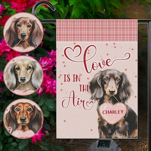 May include: A garden flag and three round ornaments featuring dachshunds. The flag reads "Love is in the Air" with a dachshund holding a heart-shaped sign that says "Charley". The ornaments have dachshund portraits.