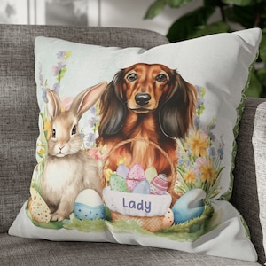 May include: A white throw pillow with a watercolor illustration of a dachshund dog and a rabbit. The dog is holding a basket of colorful Easter eggs. The pillow has the word "Lady" printed on it.