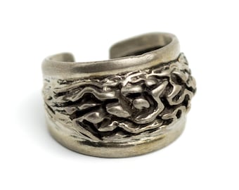 May include: A silver-toned ring with an open design. The ring features a textured, organic pattern around the band. The ring is set against a white background.
