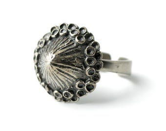 May include: A silver ring with a textured, cone-shaped design and a circular border of small, raised dots.