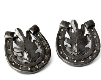 May include: A pair of black metal earrings shaped like horseshoes with a leaf design and small clear stones around the edge.