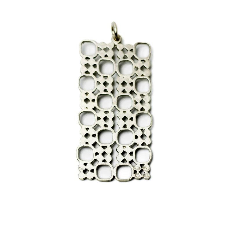 Puede incluir: Colgante rectangular plateado con dise&ntilde;o calado. El colgante presenta un patr&oacute;n repetitivo de cuadrados y rombos, con un peque&ntilde;o lazo en la parte superior para una cadena. El colgante se muestra sobre un fondo blanco.
