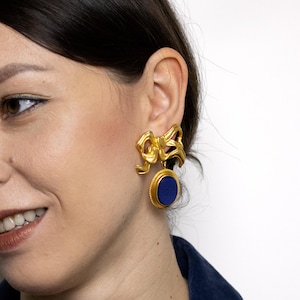 May include: Gold tone earrings with a blue stone and a bow design.