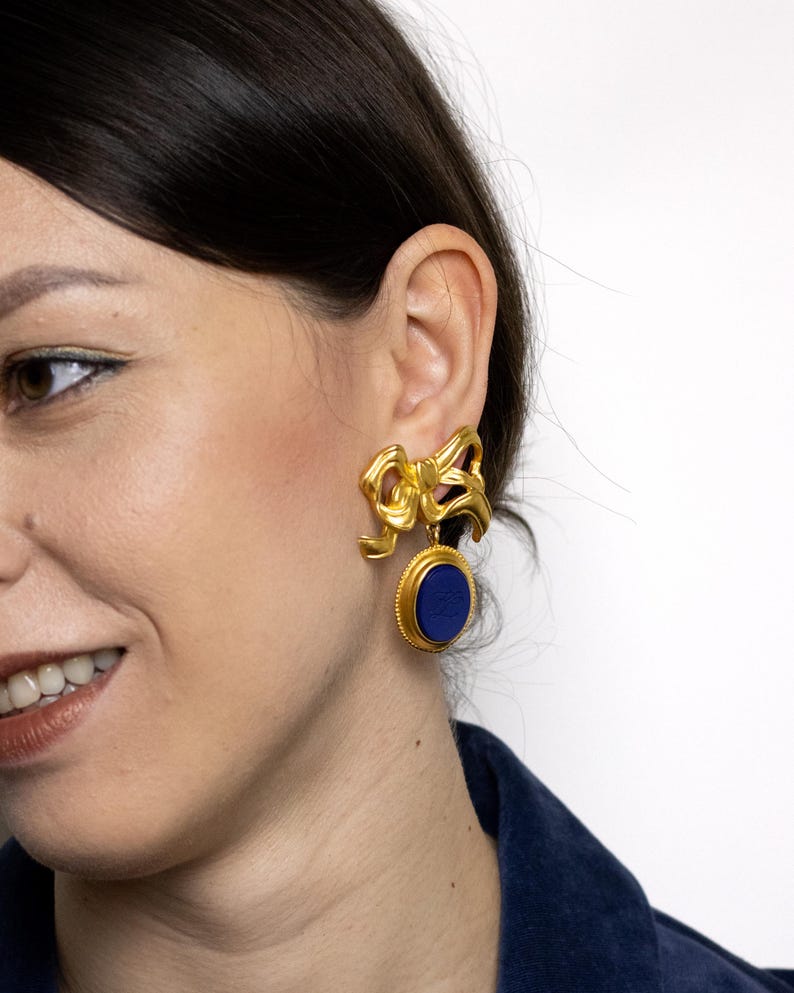 May include: Gold tone earrings with a blue stone and a bow design.