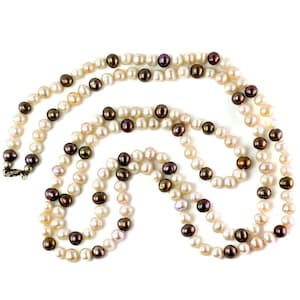 May include: A long, layered pearl necklace with a mix of white, cream, and dark brown pearls. The necklace has a silver clasp and is displayed against a white background. The pearls are oval-shaped and vary in size.